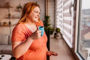 plus-size-redhead-woman-smiling-holding-coffee-looking-out-window